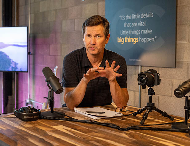 Man standing at a table giving a podcast coaching consultation