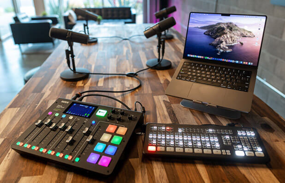 Podcast studio setup with a mixing console, microphones on boom arms and a laptop on a wooden desk