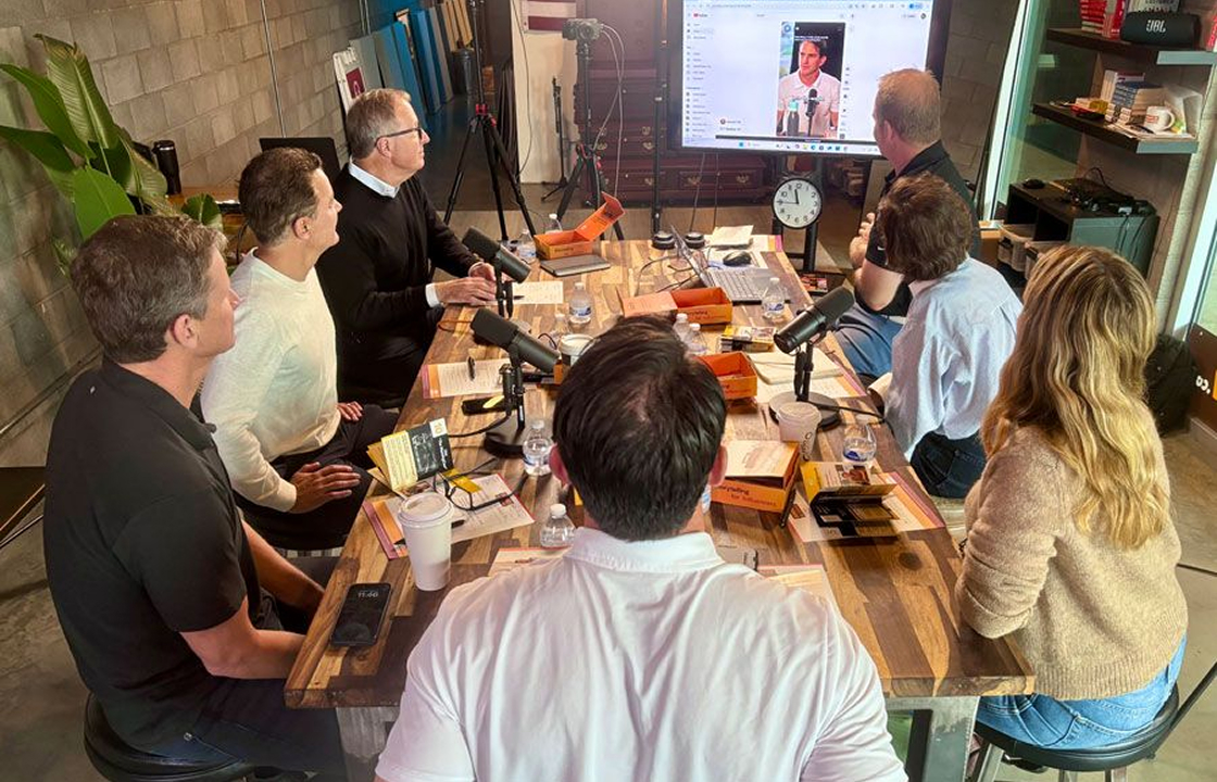 Business professionals gathered around a conference table during a podcast recording session with microphones and a presentation screen